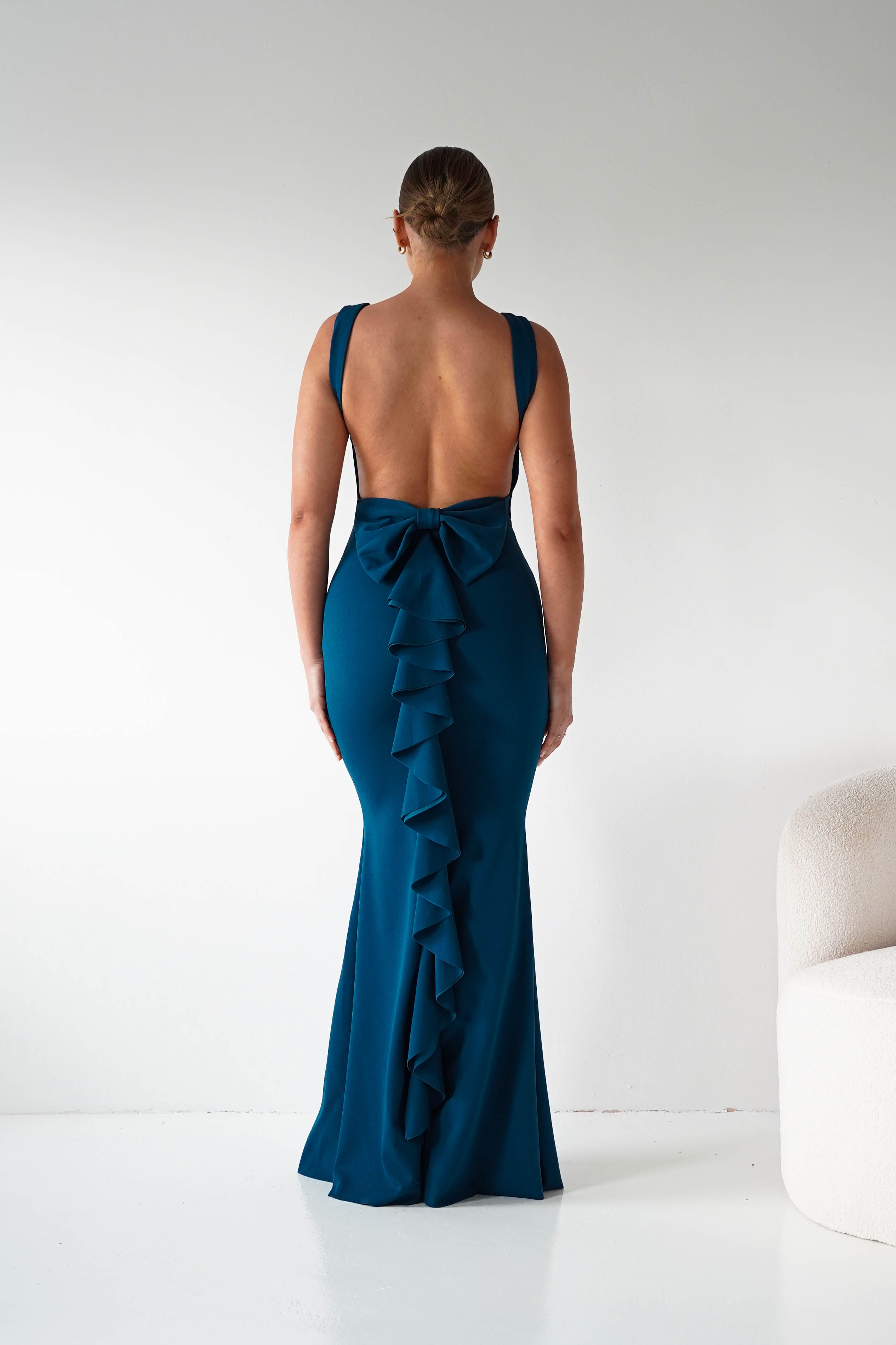 Woman wearing a teal evening gown with ruffled details on a white background