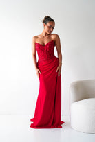 Woman in a red evening gown standing against a white background