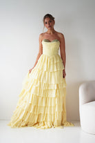 Woman wearing a yellow strapless gown with ruffled layers against a white background