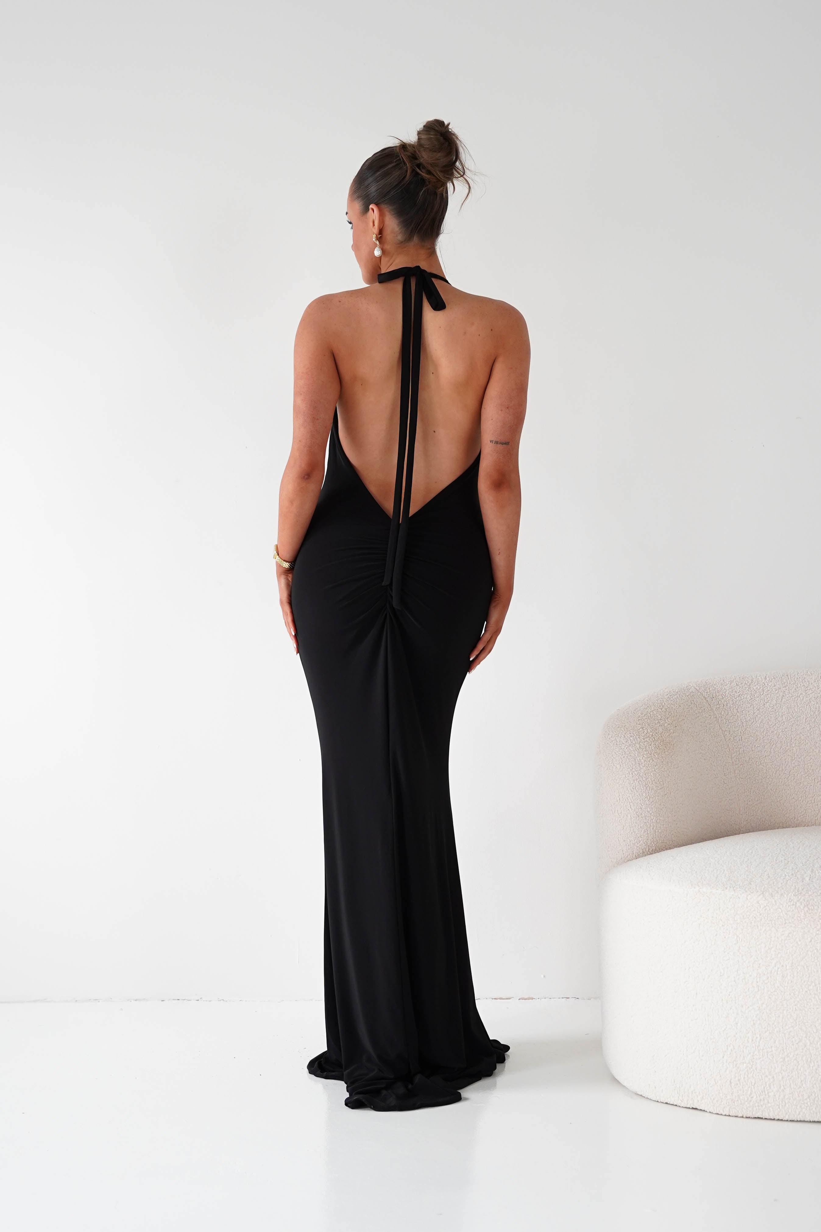 Woman wearing a black evening gown with a high slit and open back on a white background