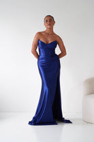 Woman wearing a blue strapless gown with a slit on a white background