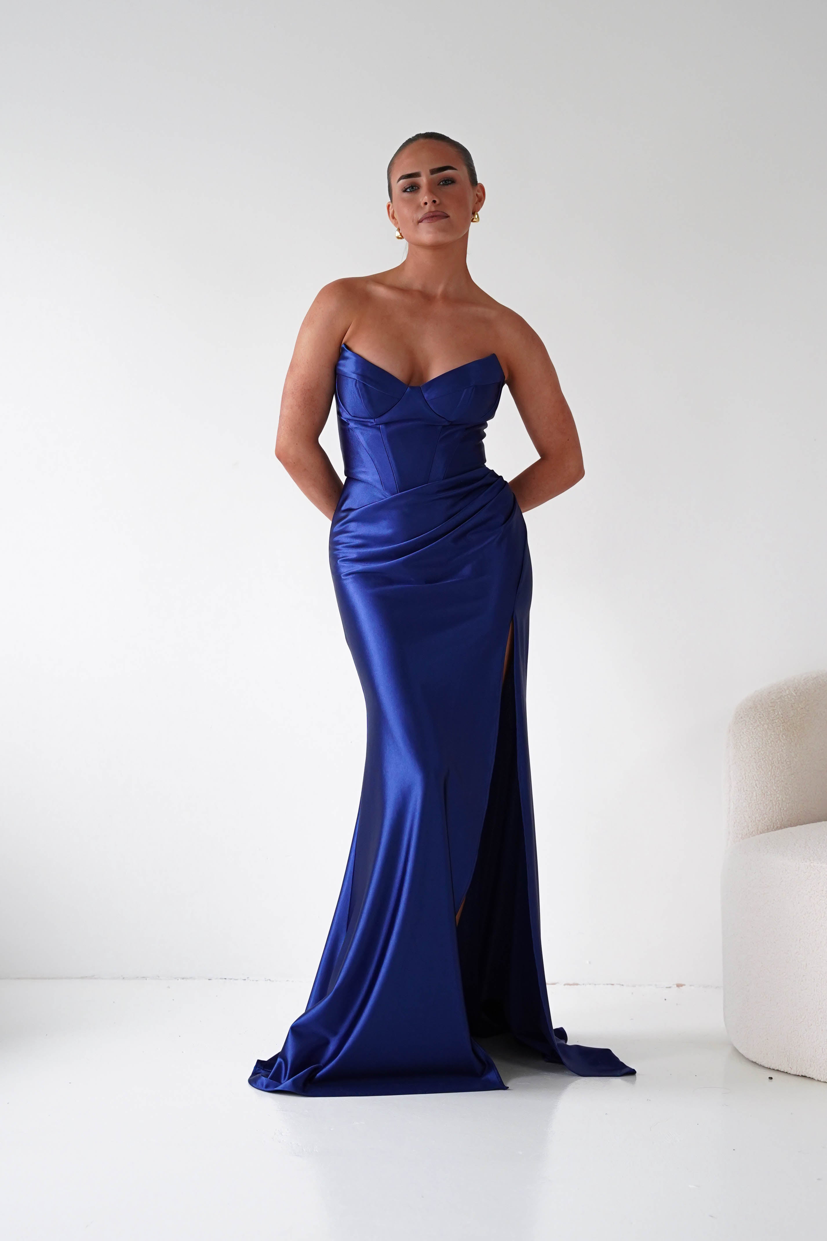 Woman wearing a blue strapless gown with a slit on a white background