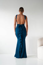 Woman wearing a teal evening gown with ruffled details on a white background