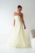 Woman wearing a strapless, light-colored evening gown against a plain background