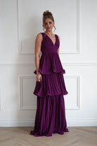Woman wearing the Vina tiered pleated layered maxi dress in plum with a deep V-neckline, flowing pleated tiers, and floor-length elegant silhouette.