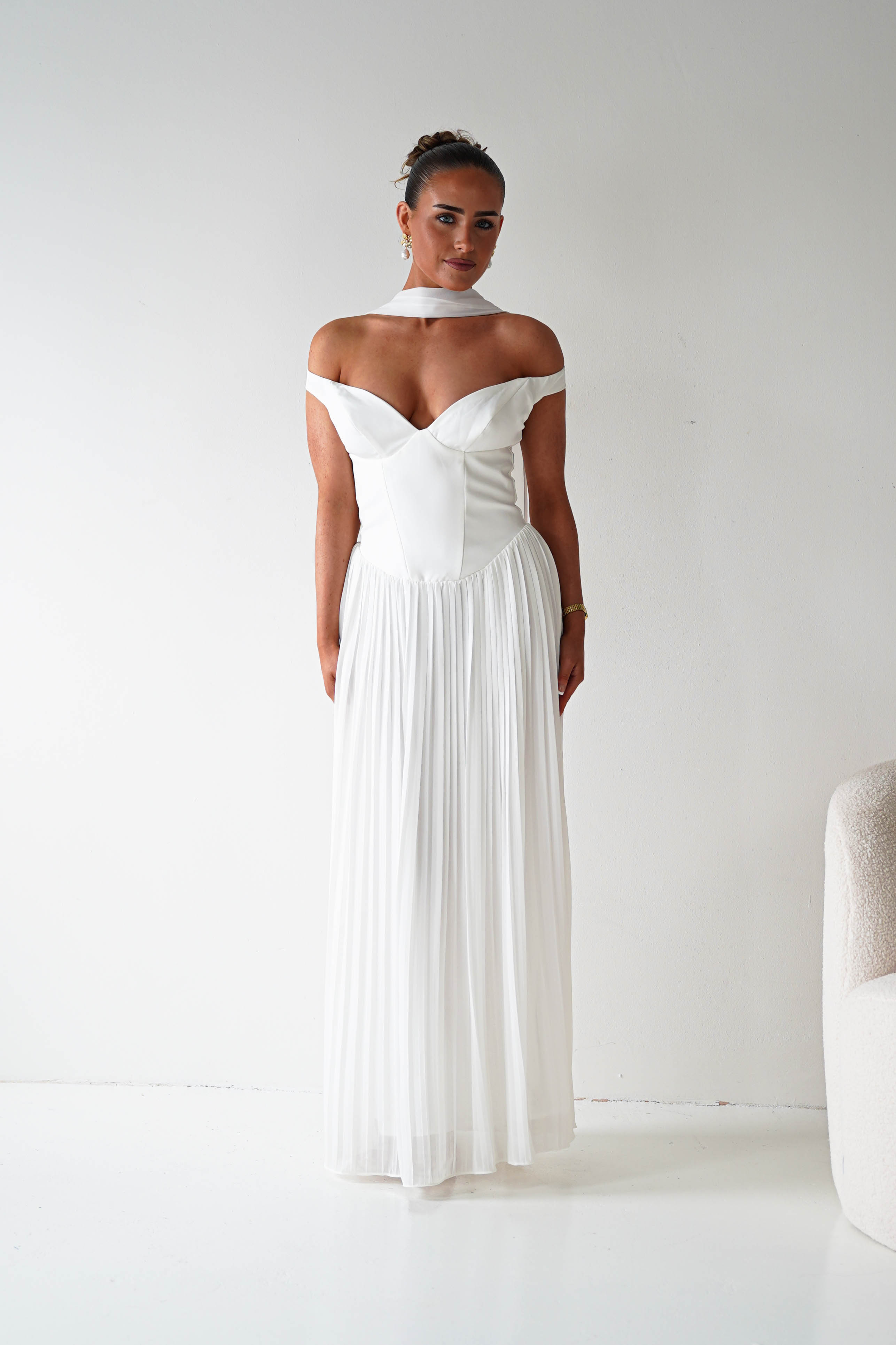 Woman wearing a white off-shoulder dress in a minimalistic room.